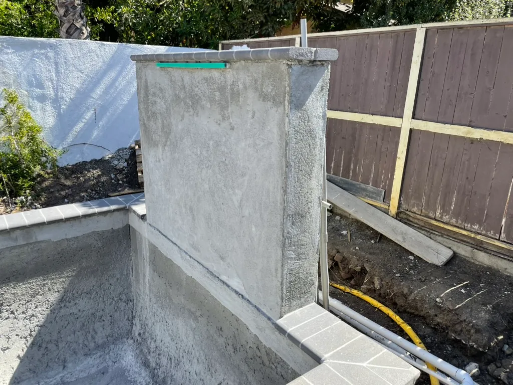 The waterfall wall shell at the end of the pool, with the gas line in the trench beside it