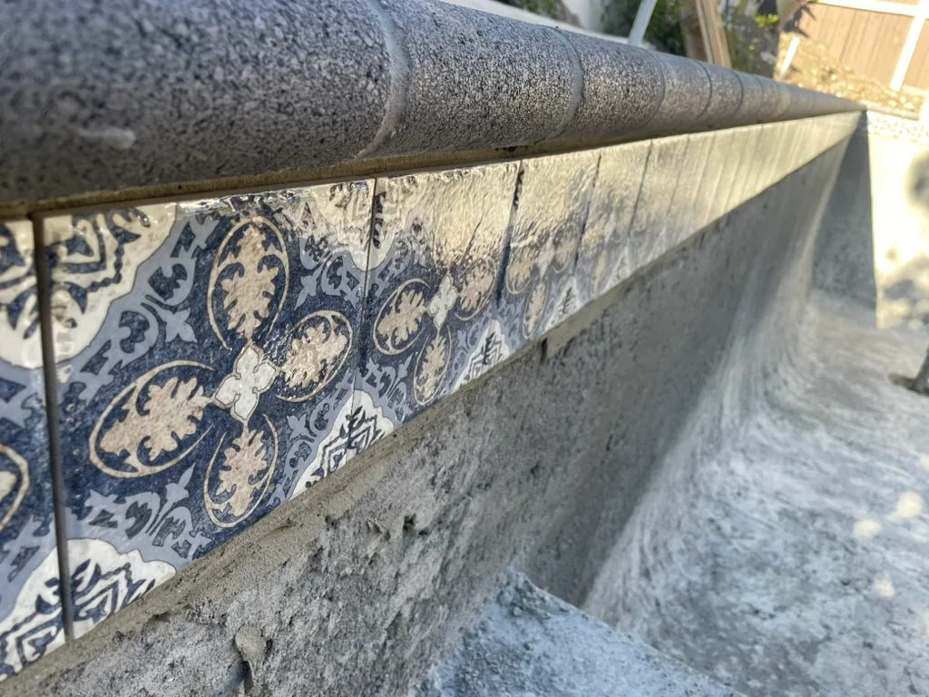 Blue and cream patterned waterline tile under grey bullnose coping