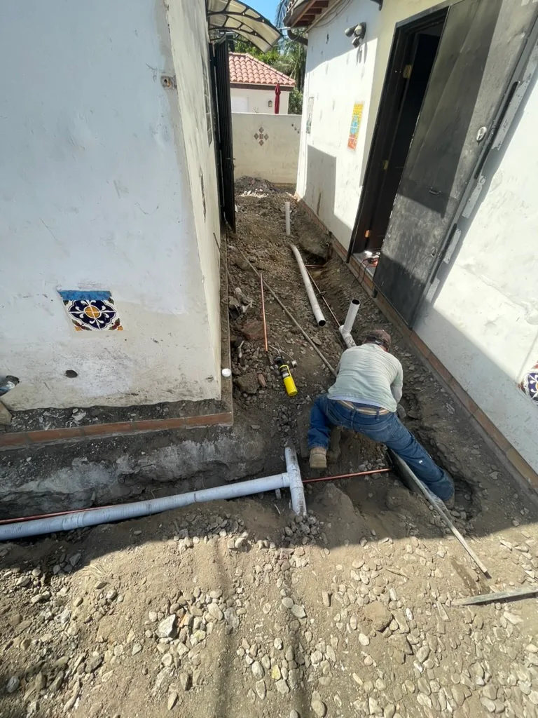 A trench through rocky soil along a narrow side passage, with new pipes laid in it
