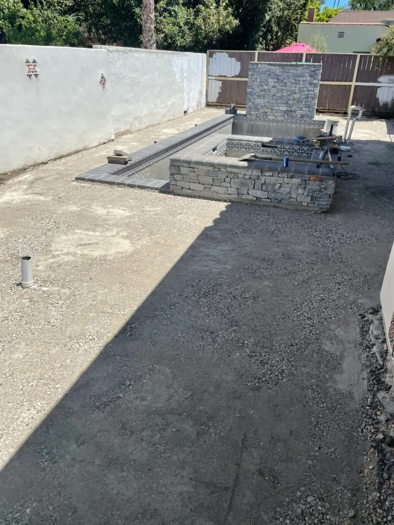 The yard graded with a gravel base around the pool, with the spa and waterfall wall faced in stone