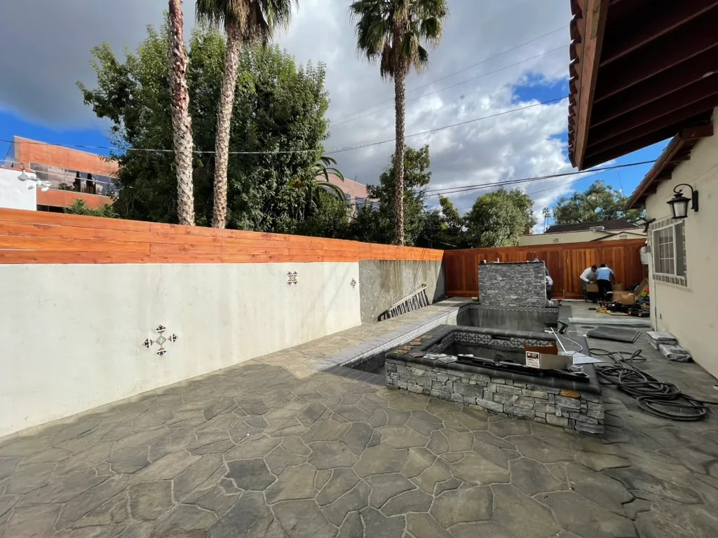 A white plastered perimeter wall with small decorative tiles and a wood fence above it