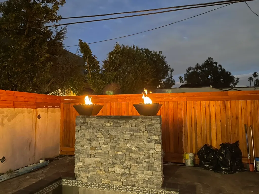 Two fire bowls lit on top of a stone-faced waterfall wall at dusk