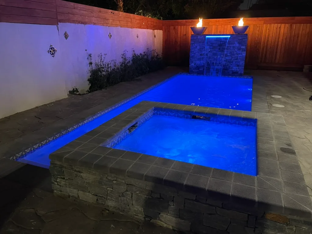 The pool and spa lit blue at night, with fire bowls lit on the waterfall wall