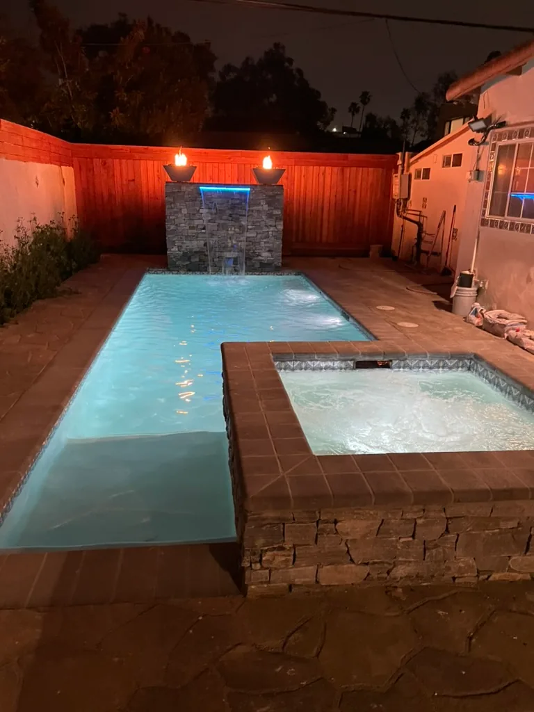 The pool lit white at night, with the waterfall running and fire bowls lit