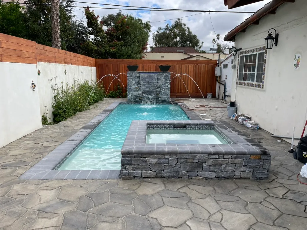 The finished pool and spa from the patio, with deck jets arcing into the pool