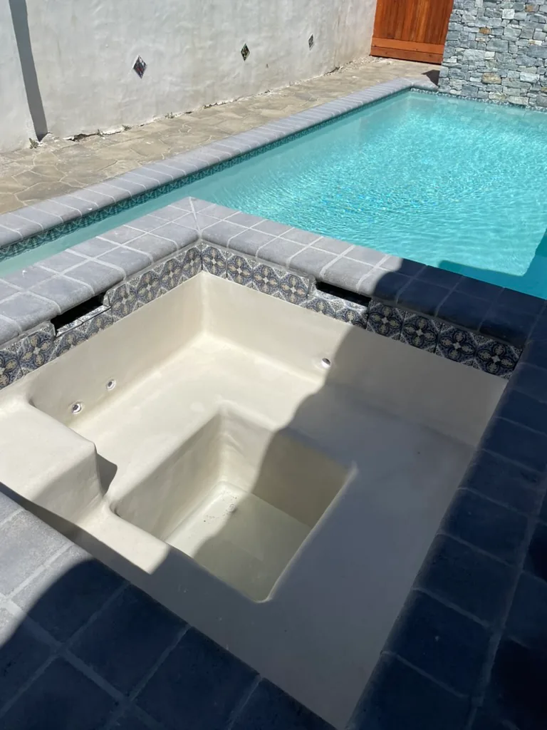 The inside of the spa in light plaster, with a bench and jets under patterned waterline tile