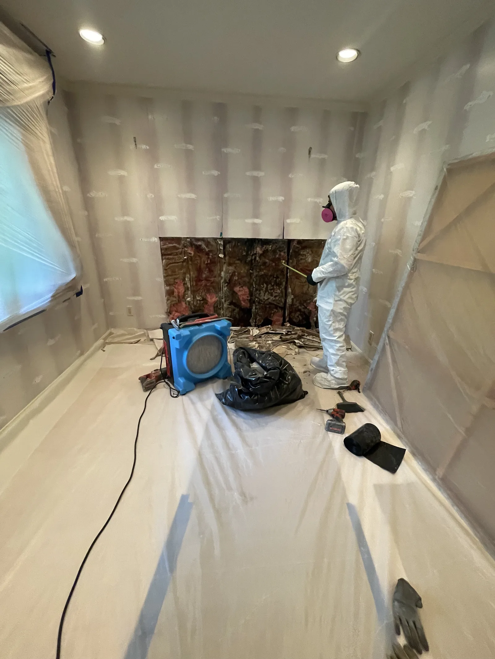 A worker in a protective suit and respirator next to a small opening in the wall
