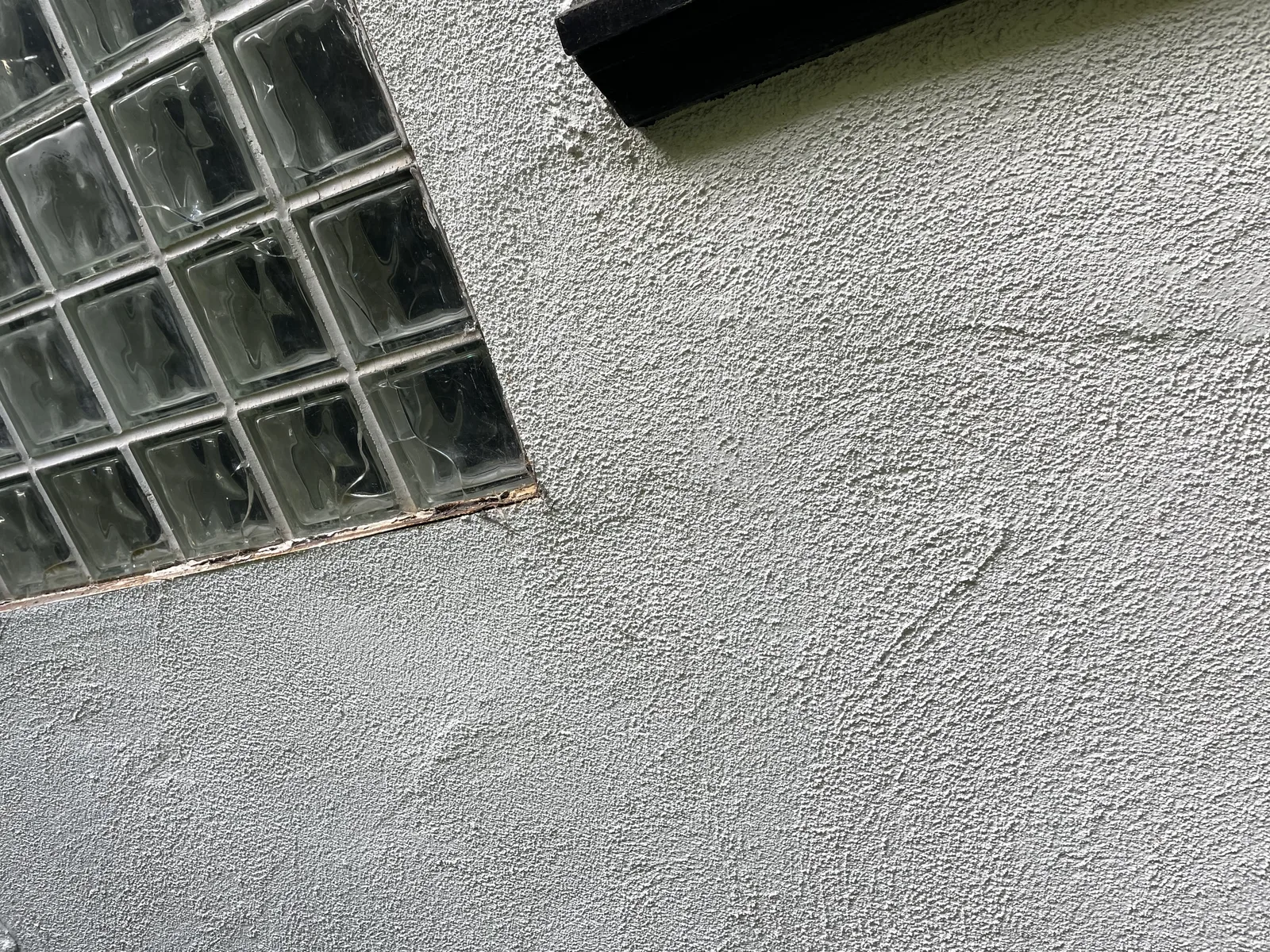 An exterior stucco wall below a second-floor glass block window