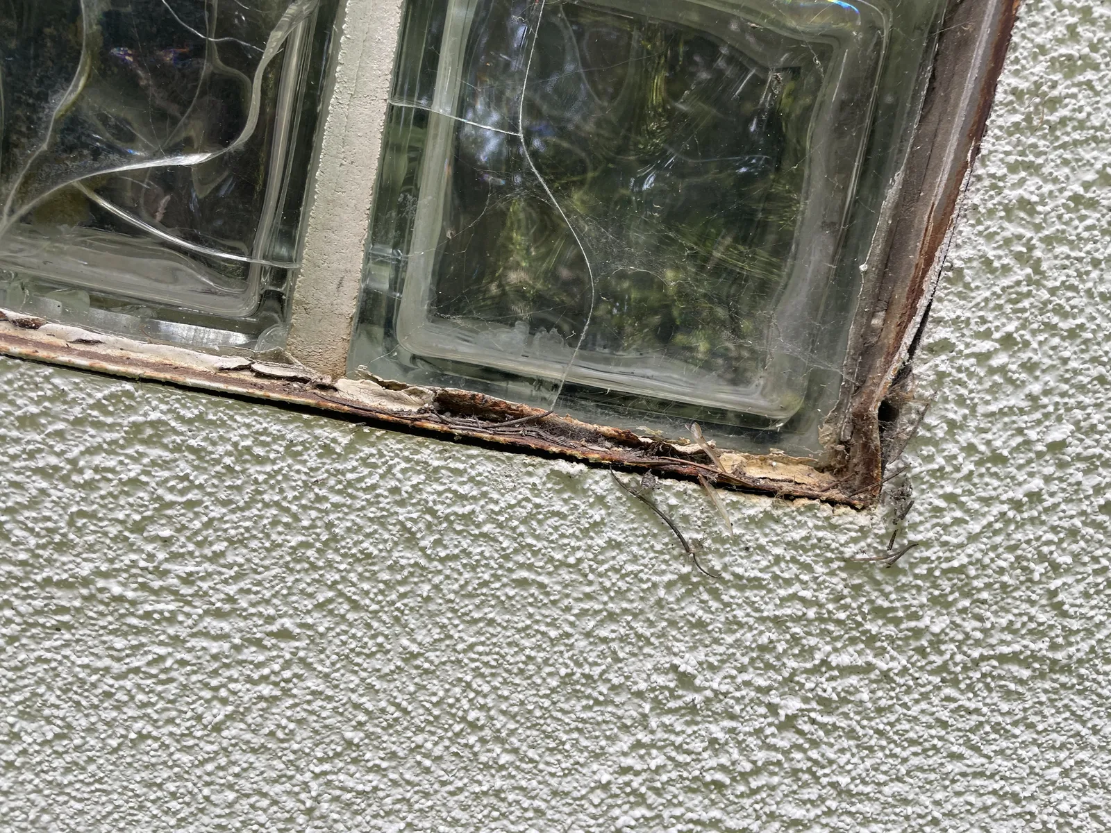 A closer view of rotted trim and cracked stucco at a window corner