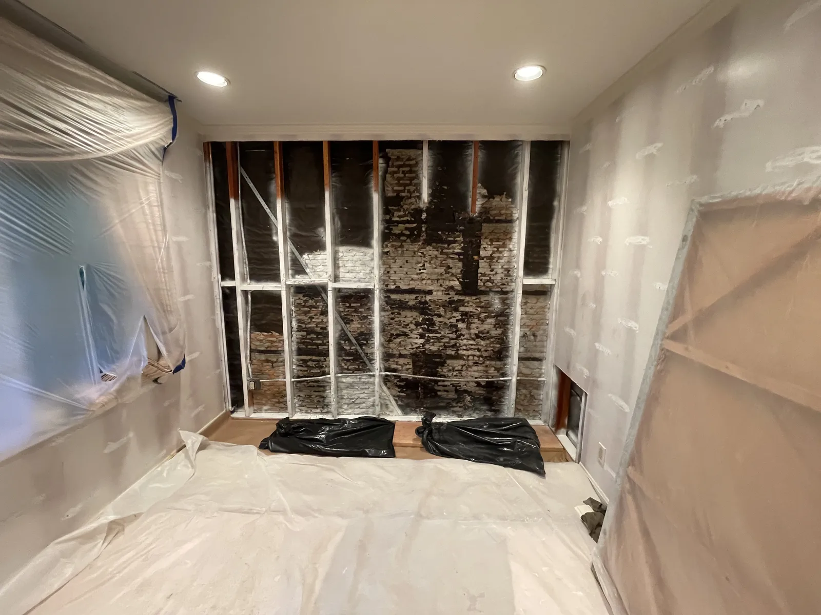 An interior wall opened to the framing and brick across the room