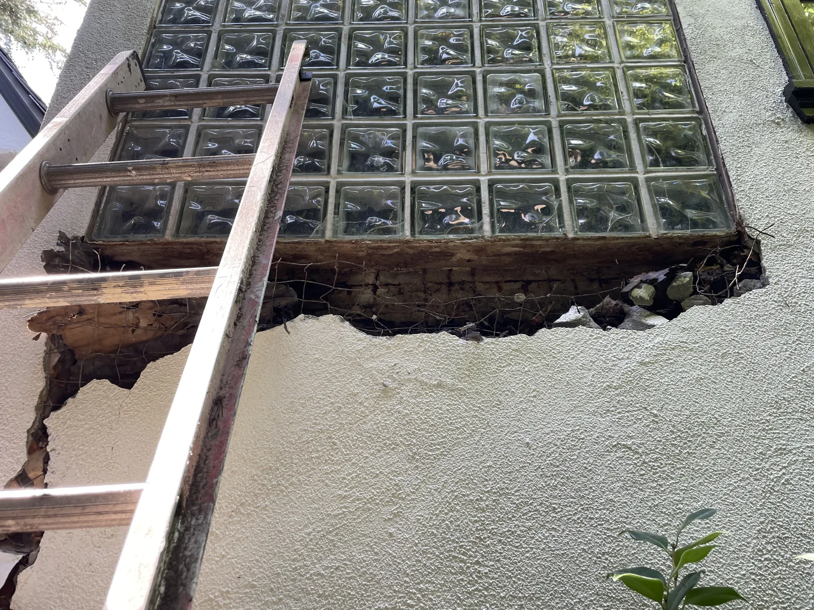 The exterior stucco cut open below a second-floor window, exposing rotted wood behind it