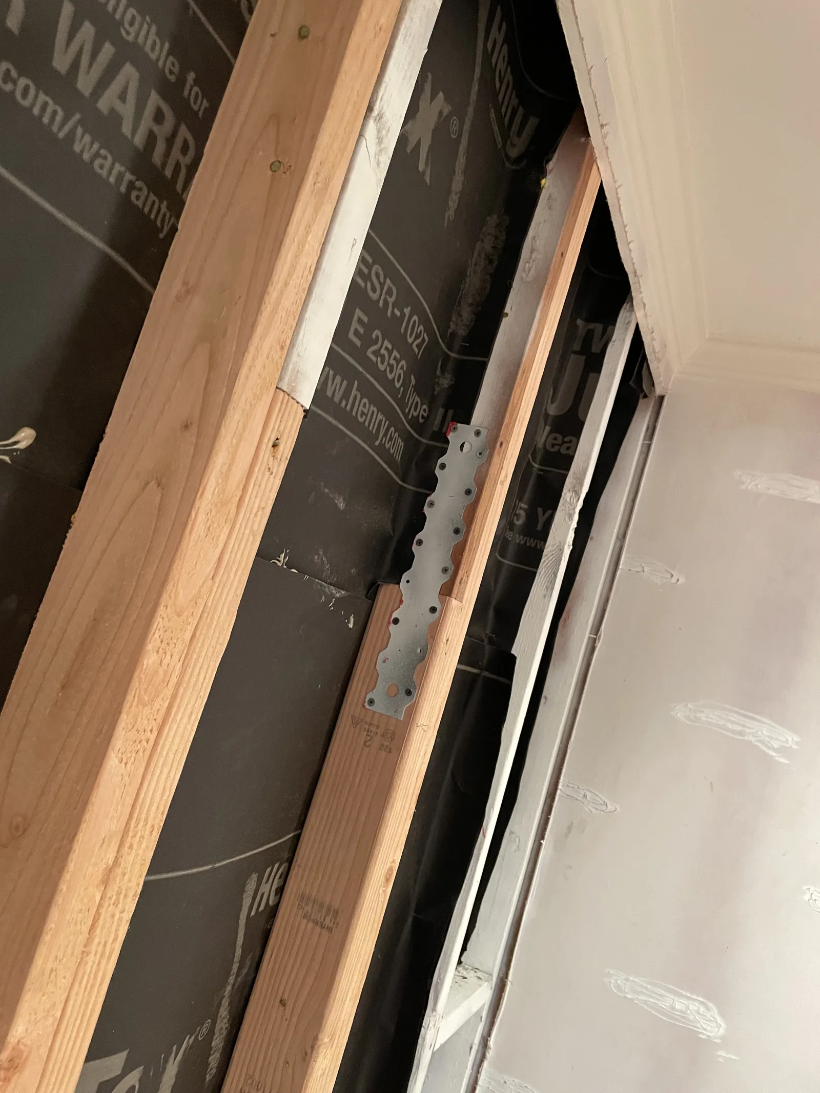 New framing next to a drywall edge, with a metal strap visible