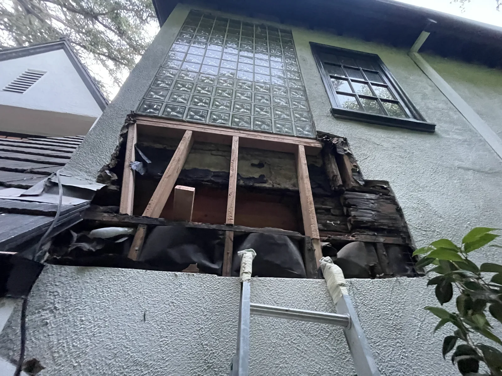 An exterior view of a second-floor window with the wall below it opened to framing