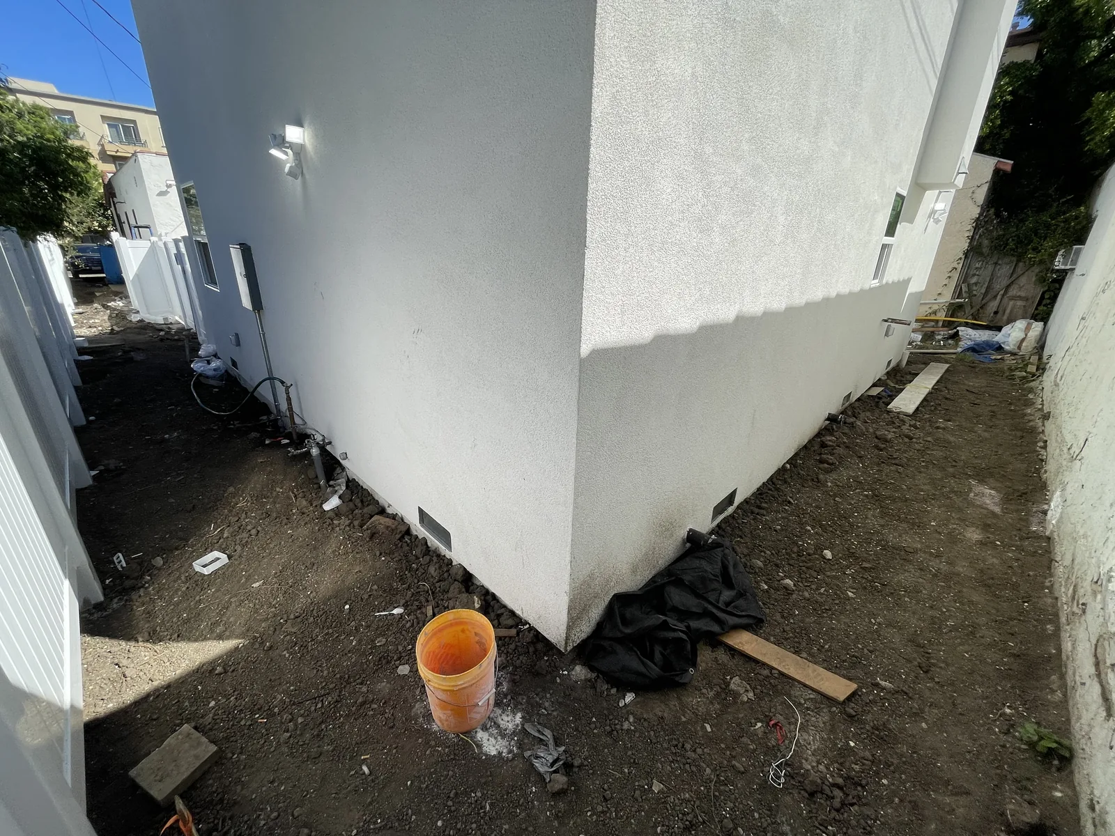 A finished stucco exterior corner with a white vinyl fence along the side yard