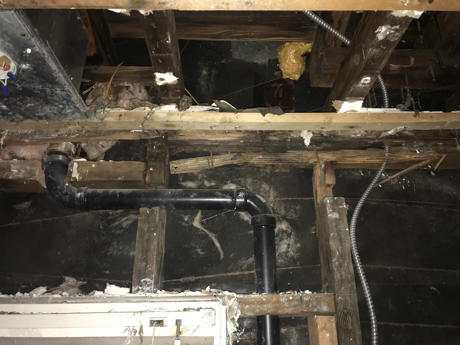 Rotted wood framing exposed under the house next to a newly installed black ABS waste pipe