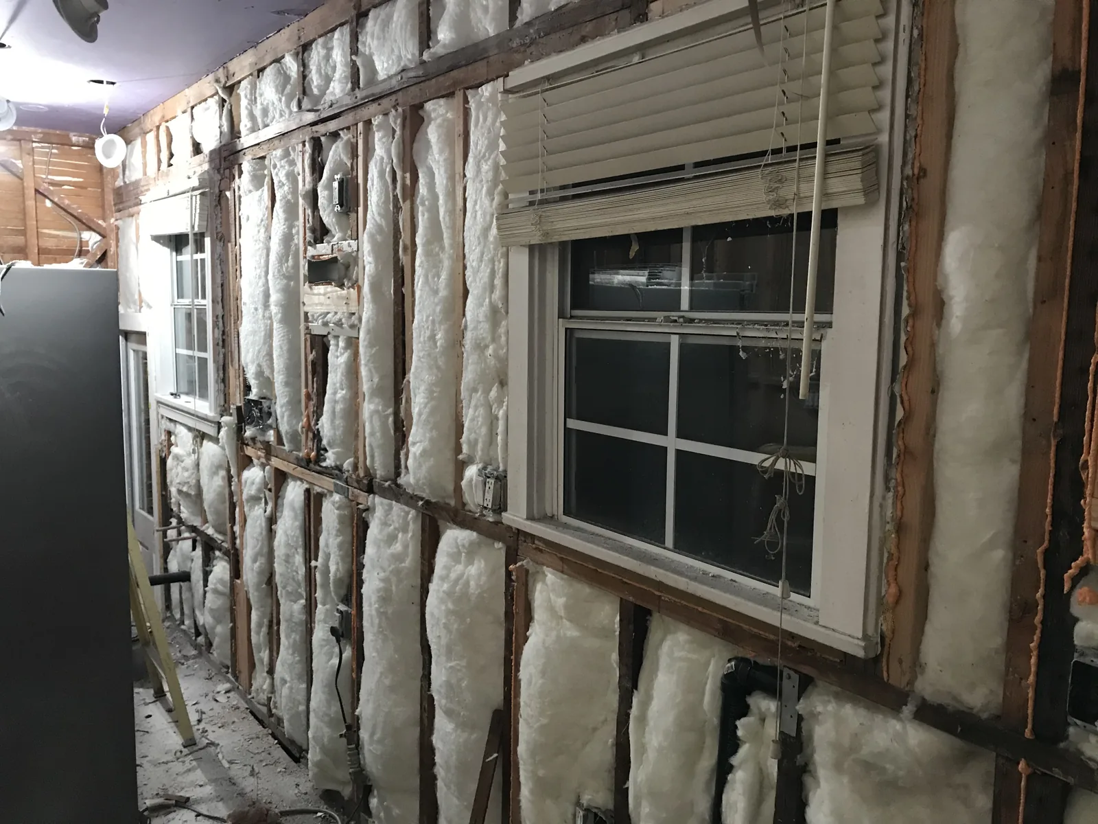 A new white window installed in the kitchen wall, surrounded by fresh insulation batts