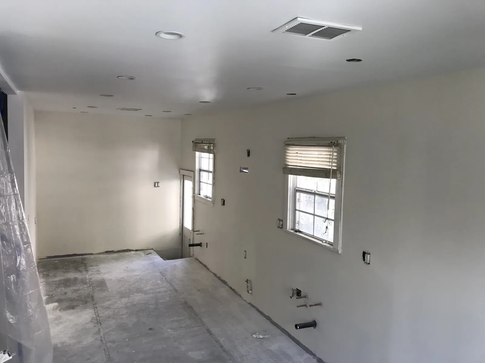 The kitchen drywalled and painted with recessed lighting, floor still bare concrete, waiting on cabinets