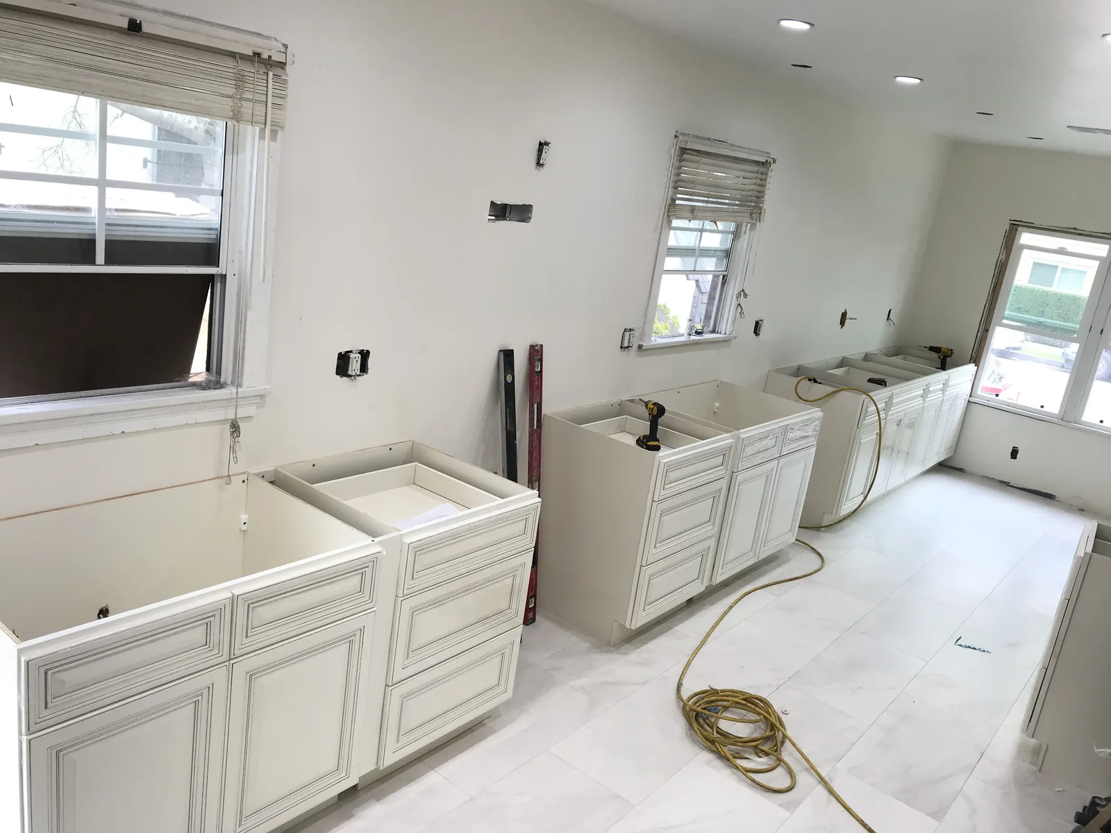 Kitchen cabinets being installed along a wall with several new windows