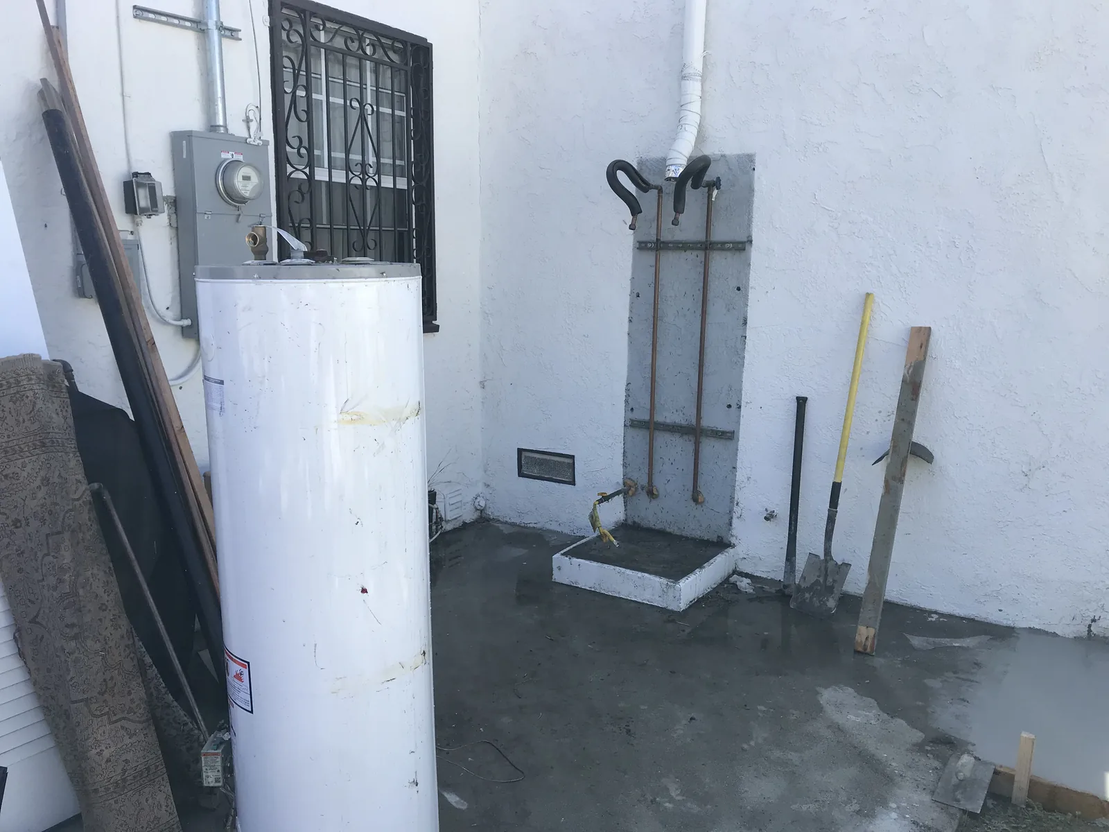 The old tank water heater removed from its exterior alcove, with a new copper and gas stub-out mounted beside it