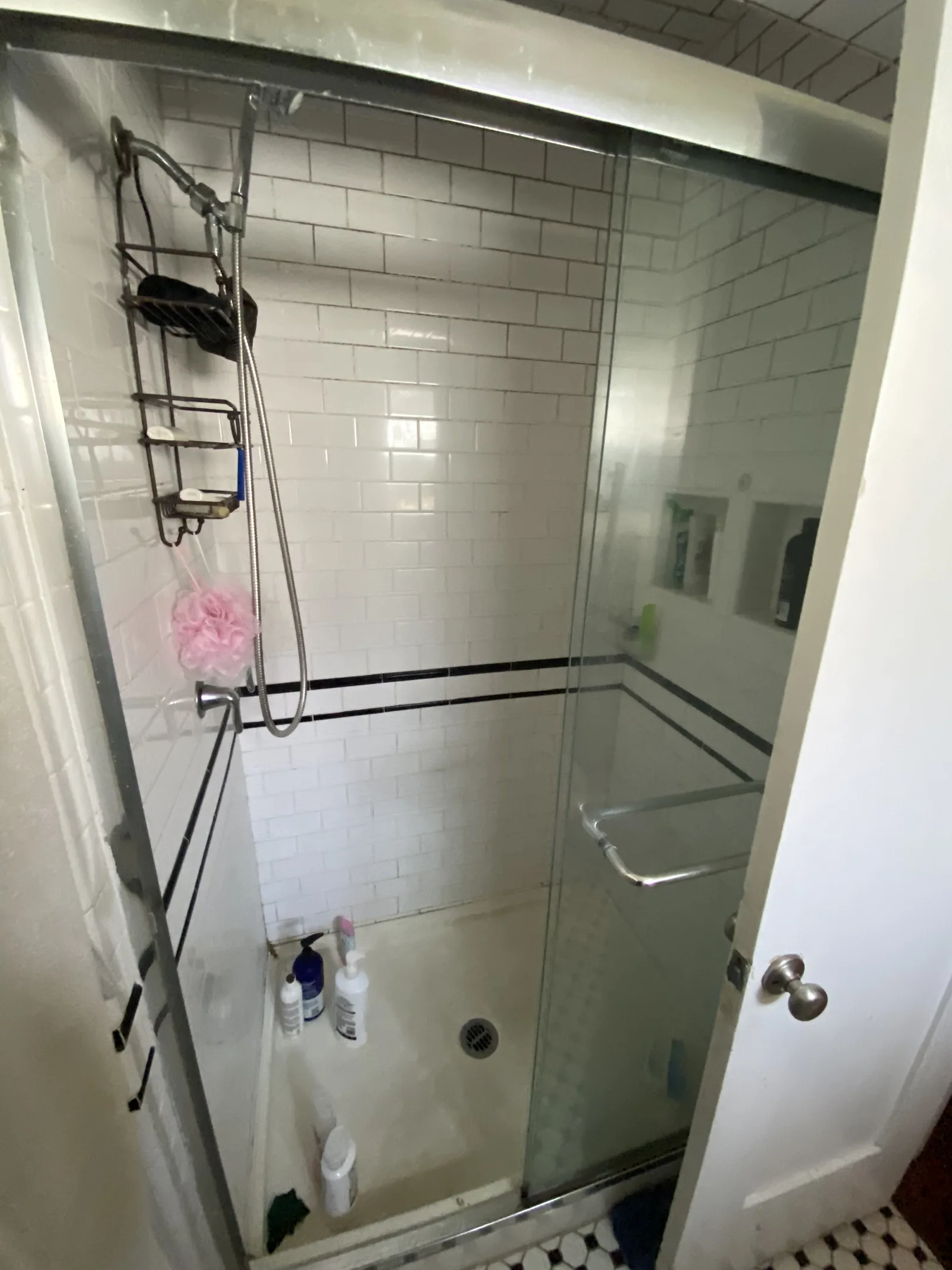 One of the original showers before renovation, with white subway tile and a black accent stripe