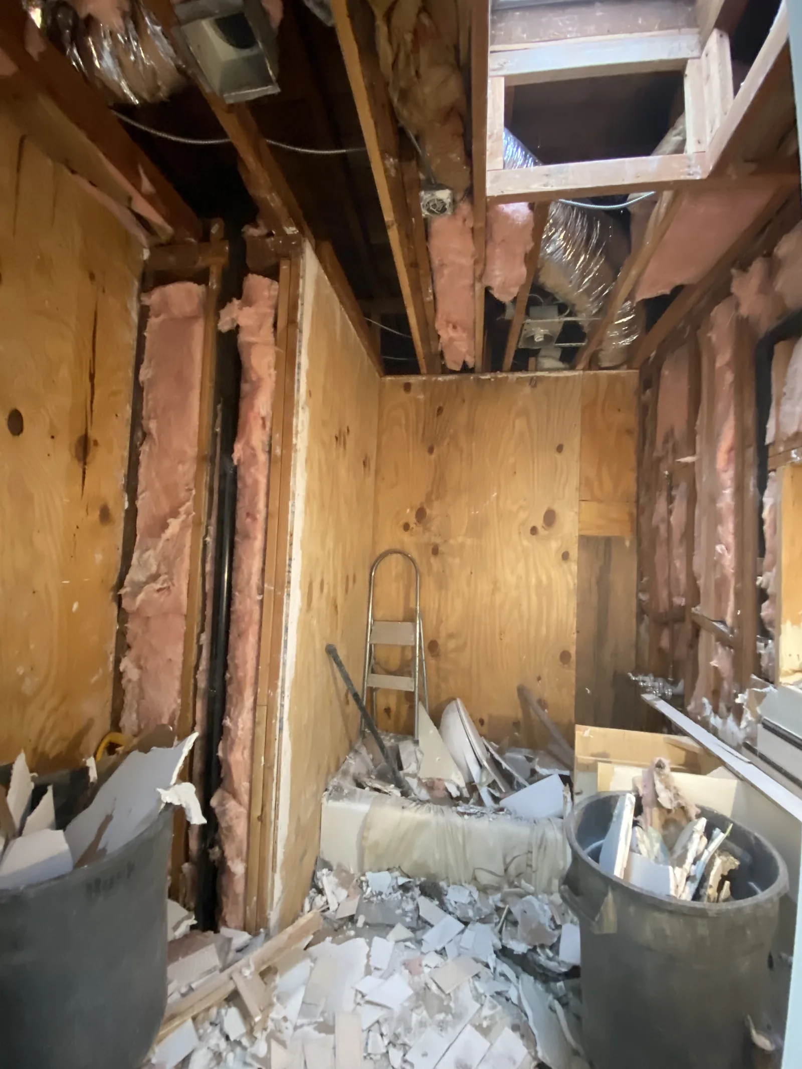 A bathroom stripped down to the studs and insulation, demolition debris on the floor