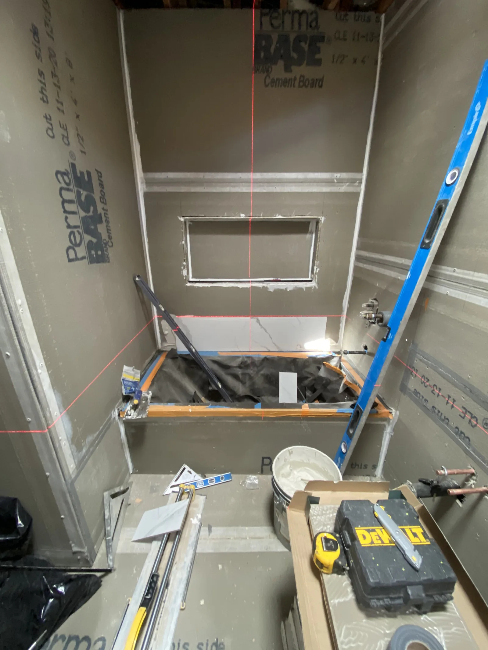 A laser level projecting reference lines onto cement board shower walls for tile layout