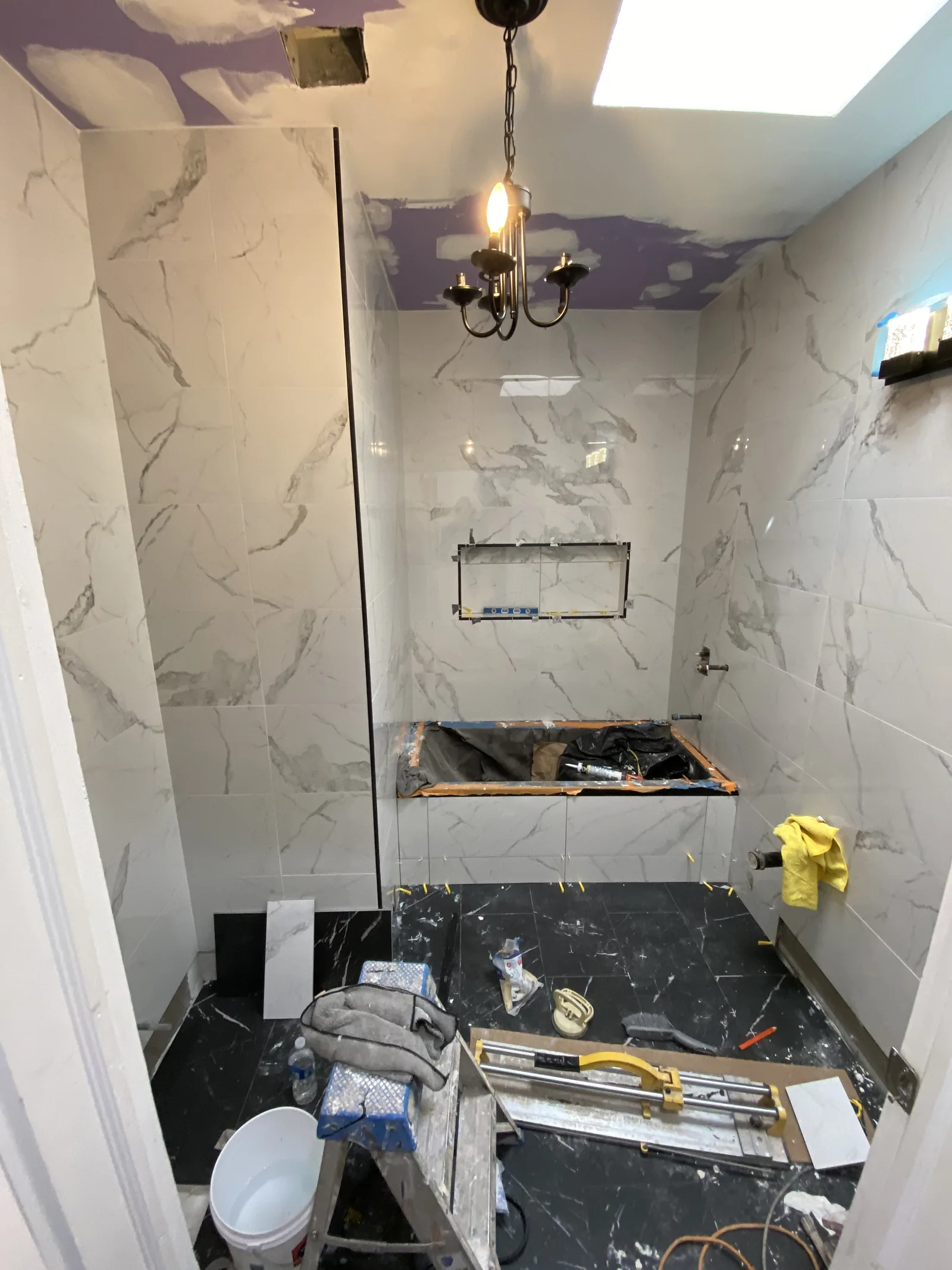 Black floor tile being installed in a bathroom with a chandelier fixture already hung overhead