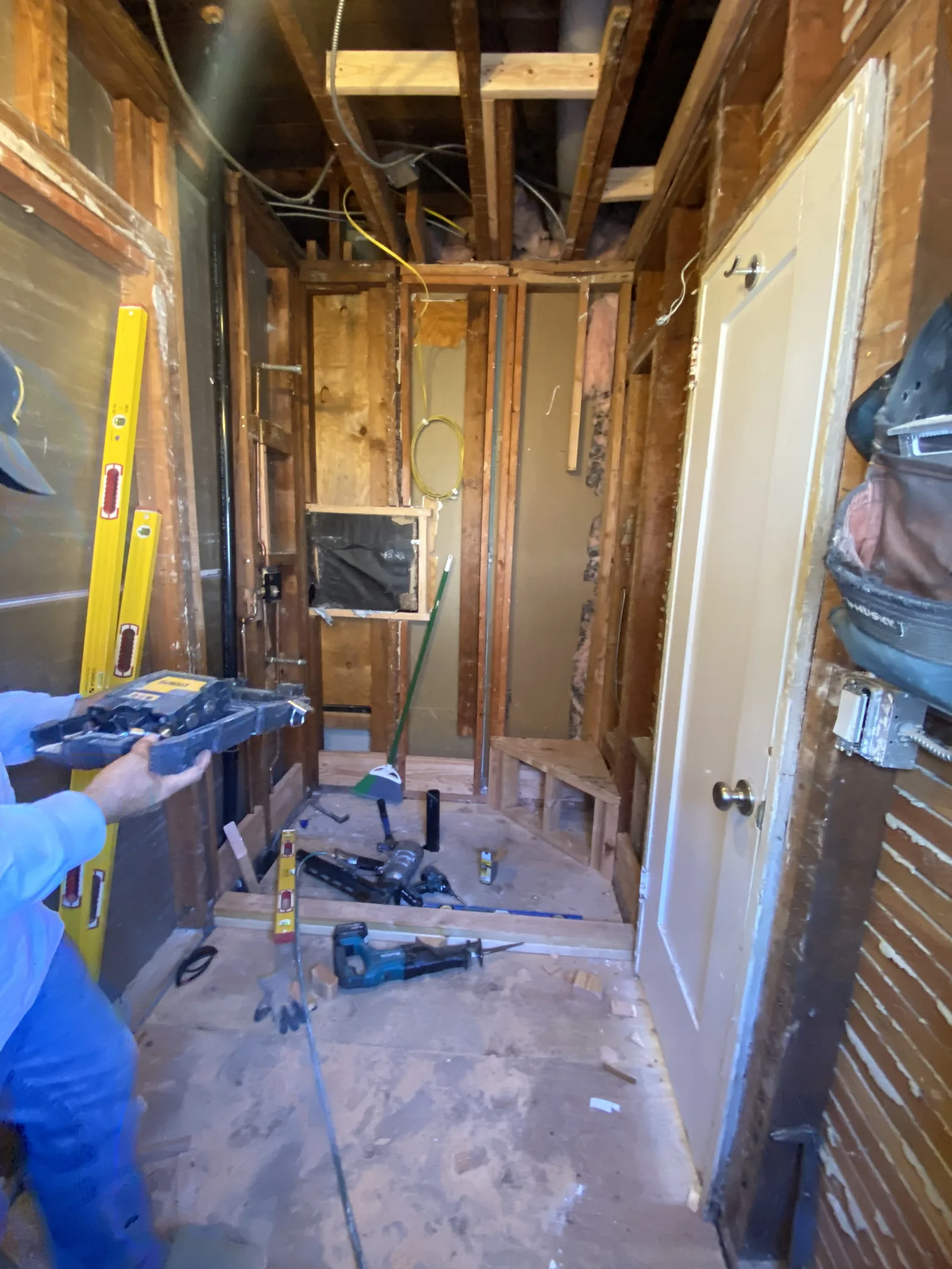 A worker with a reciprocating saw doing framing work in a gutted bathroom