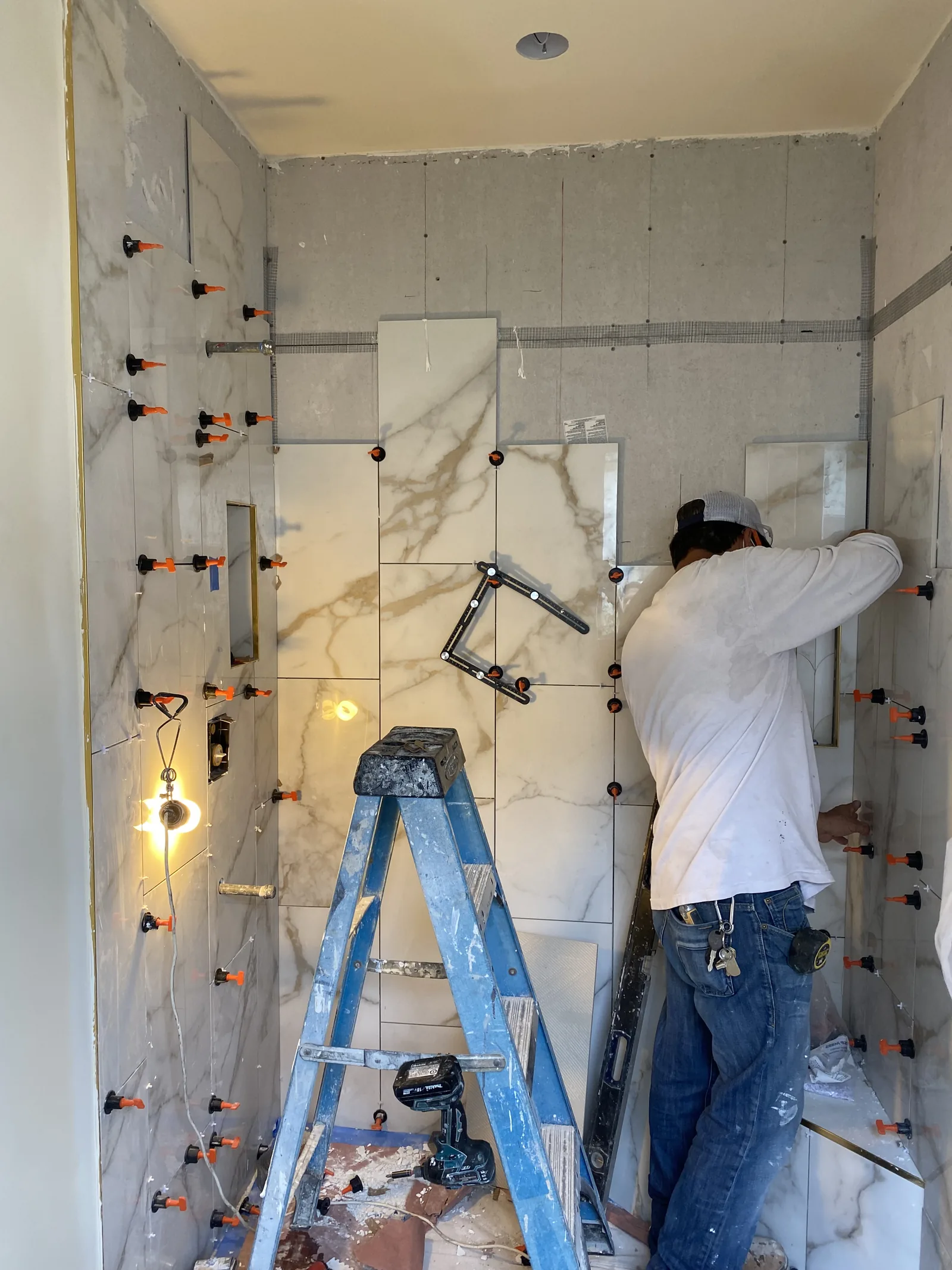 A tile installer setting large-format tile with leveling clips in a shower