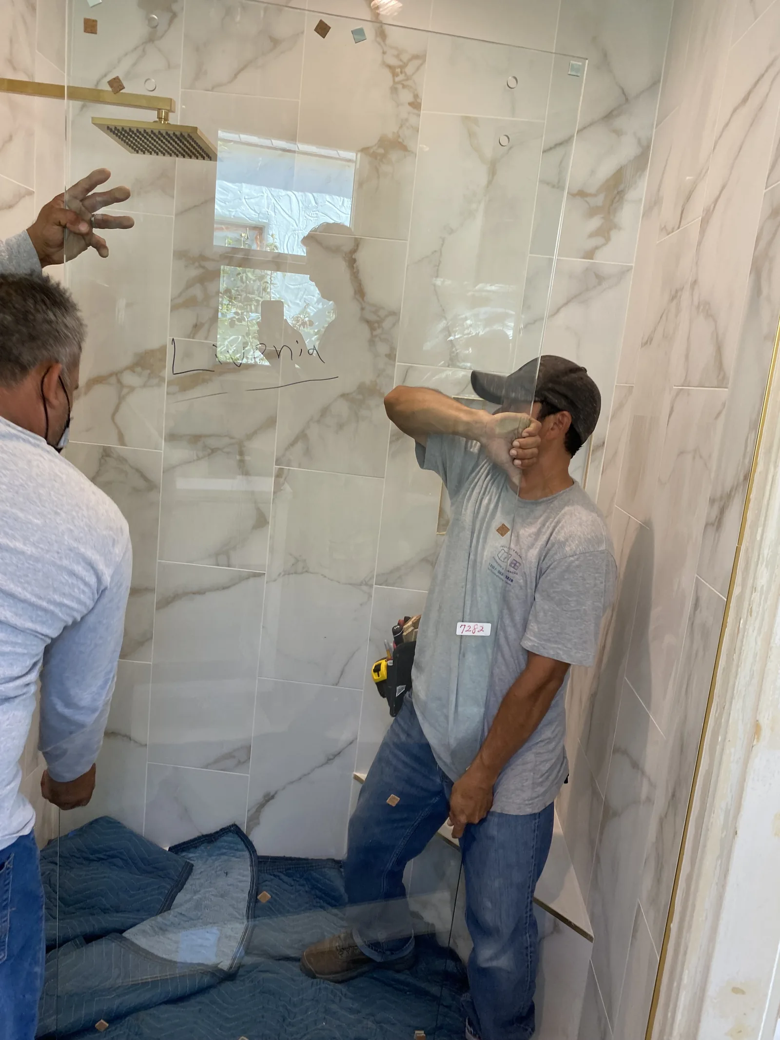 Two workers installing a glass shower enclosure with brass shower fixtures