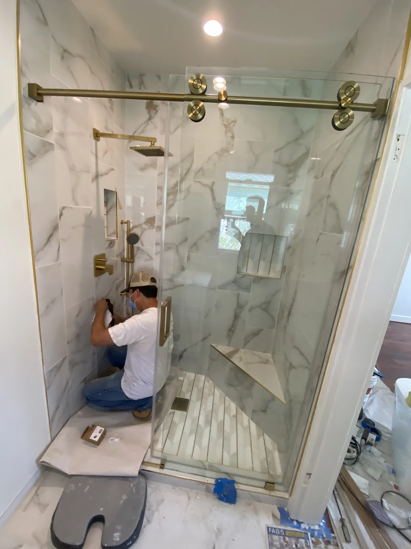 A worker installing the final glass panel on a shower with brass hardware
