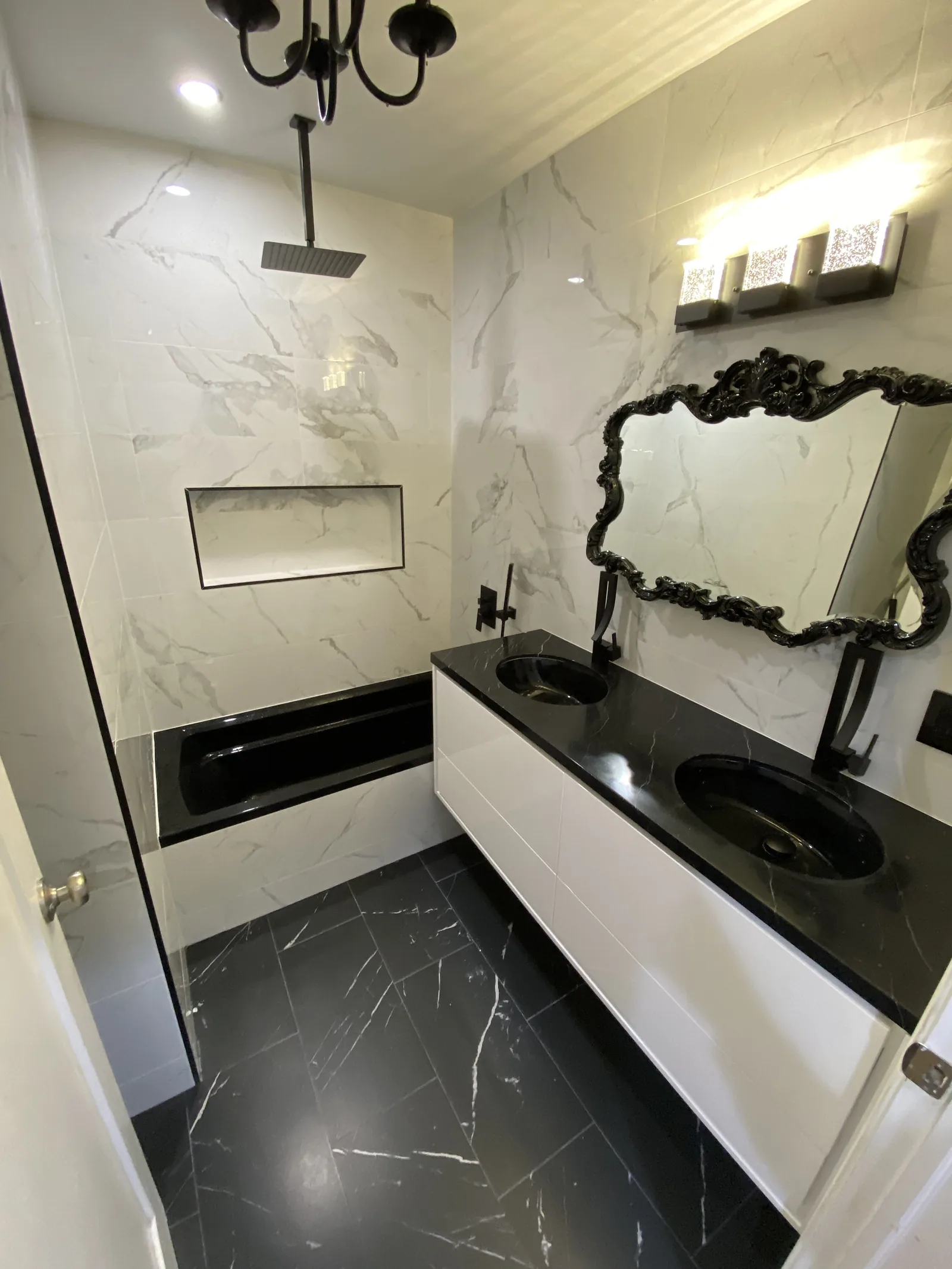 The finished primary bathroom with black and white marble, a crystal chandelier, and a freestanding tub