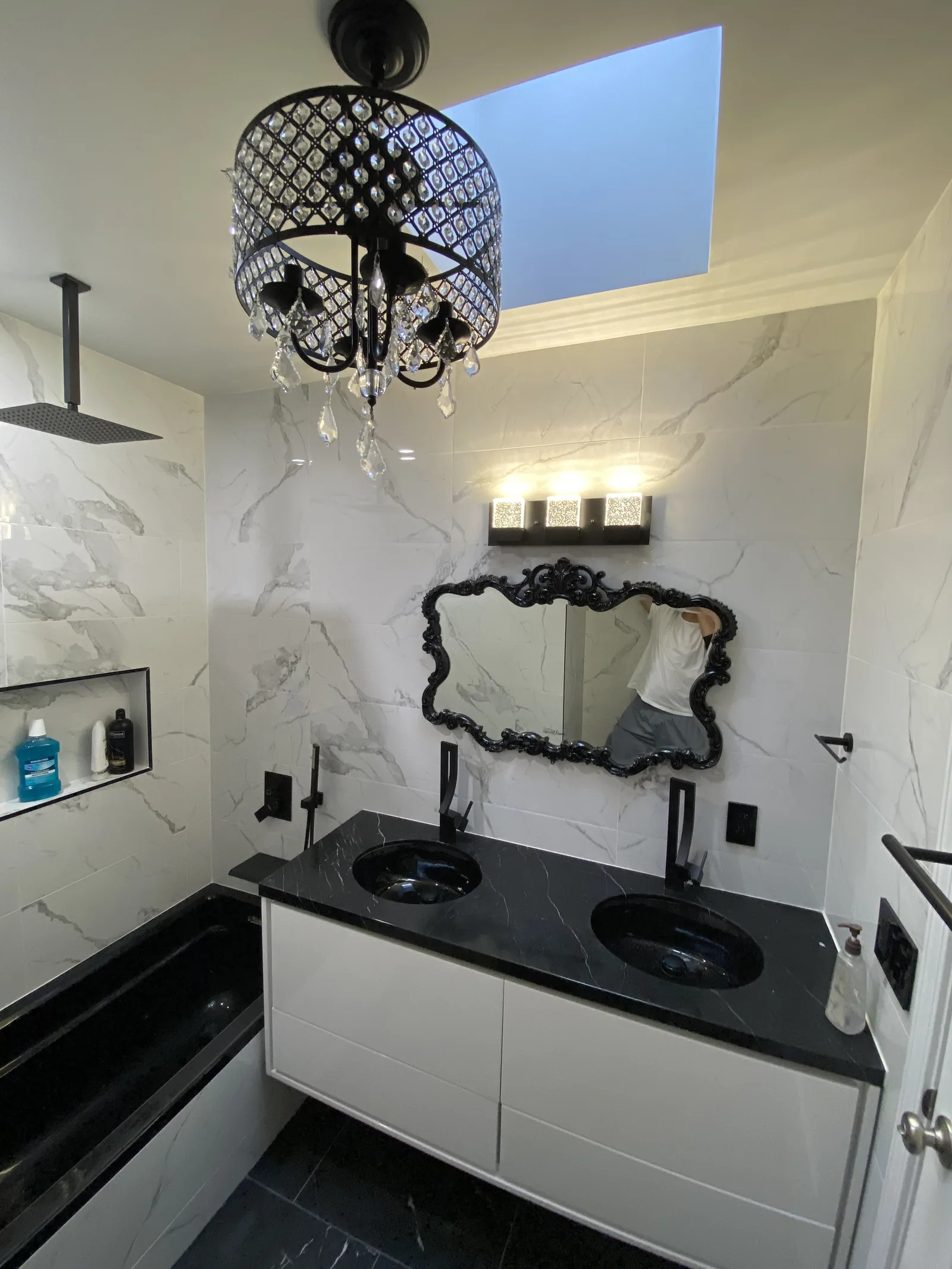 A black marble bathroom vanity with a crystal chandelier and an ornate Victorian-style mirror