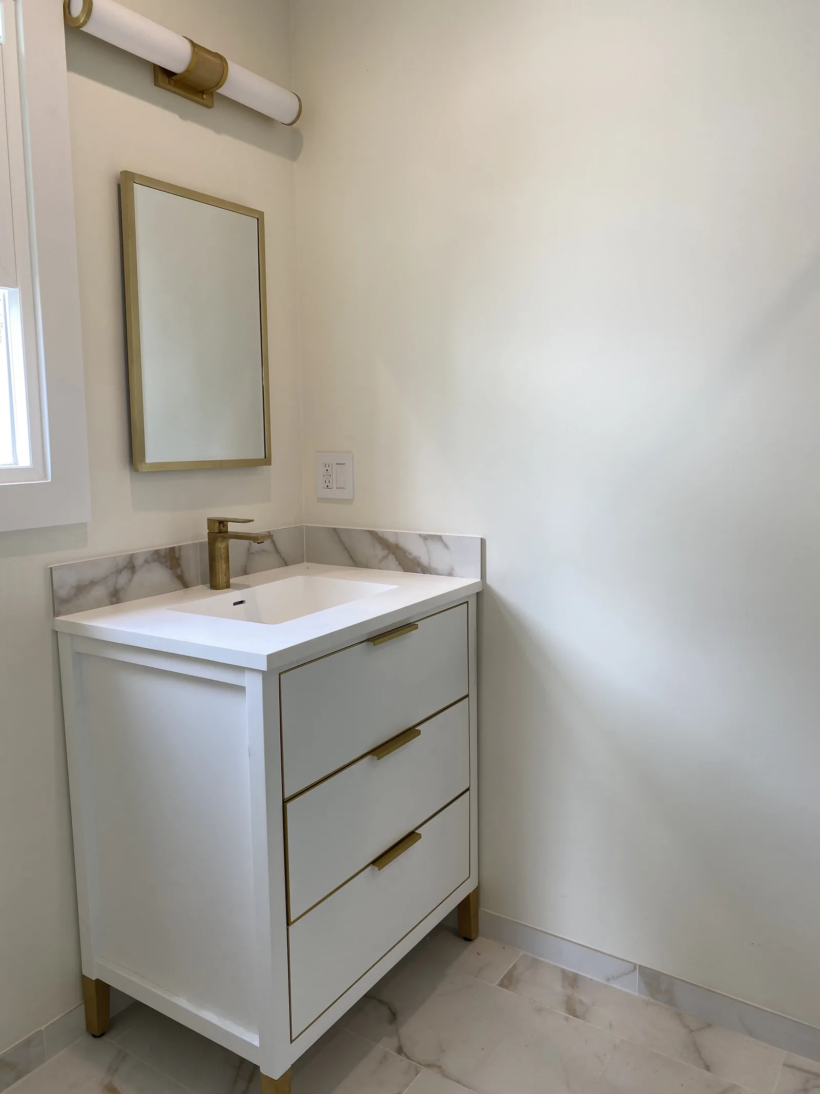 A finished bathroom vanity with brushed brass hardware and a marble backsplash