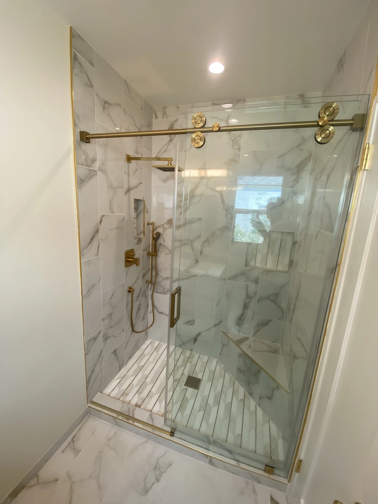 A finished bathroom shower in marble-look tile with brushed brass fixtures