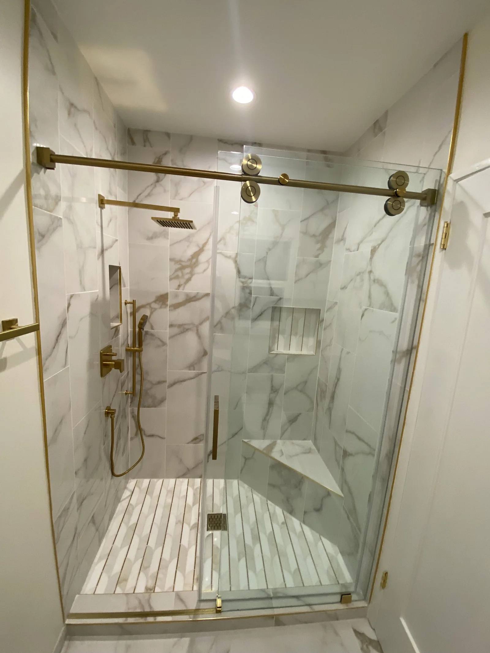 A second finished bathroom shower with matching marble-look tile and brass fixtures