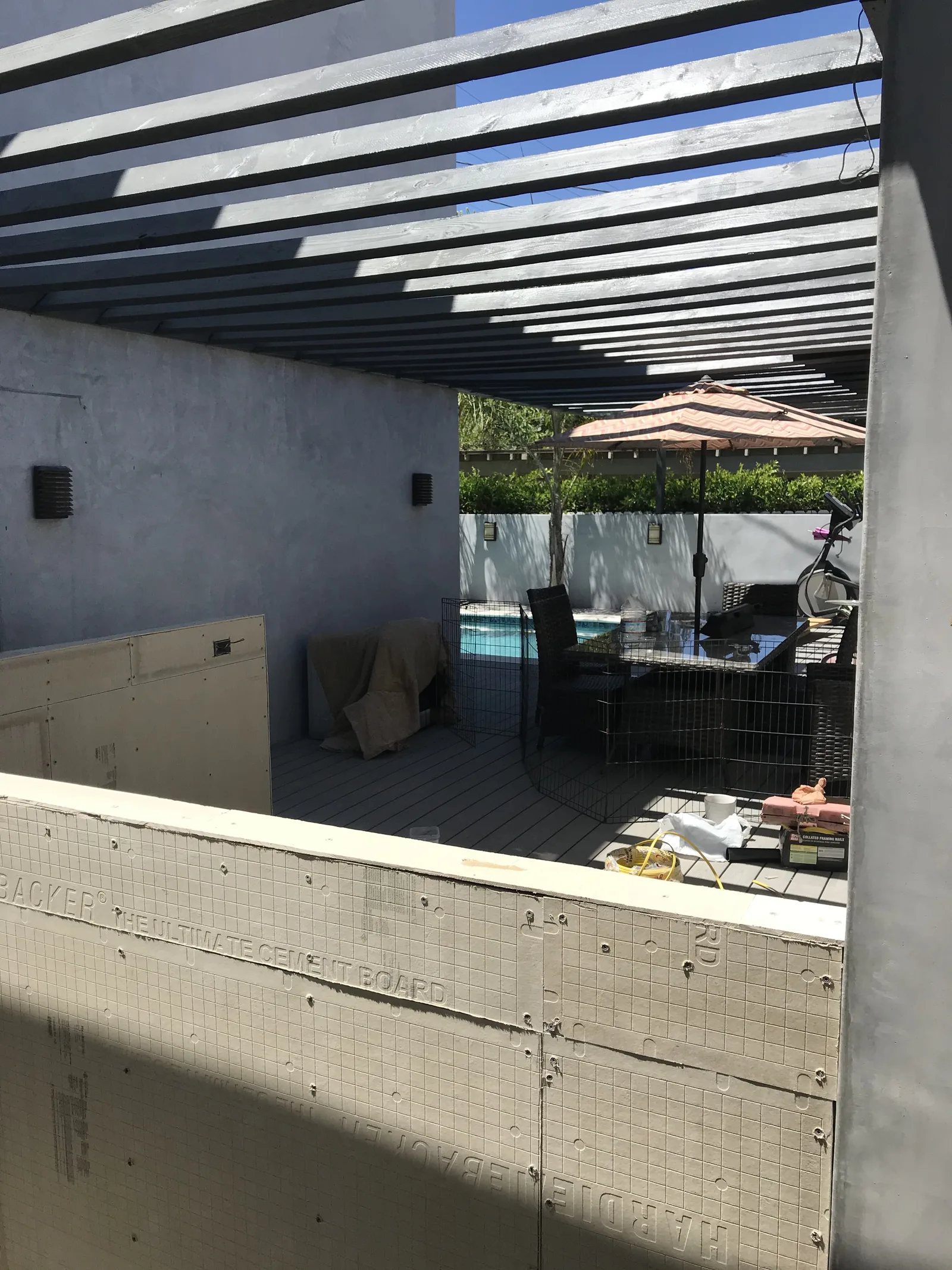 A view through an extended pergola toward a pool, with a kitchen structure starting