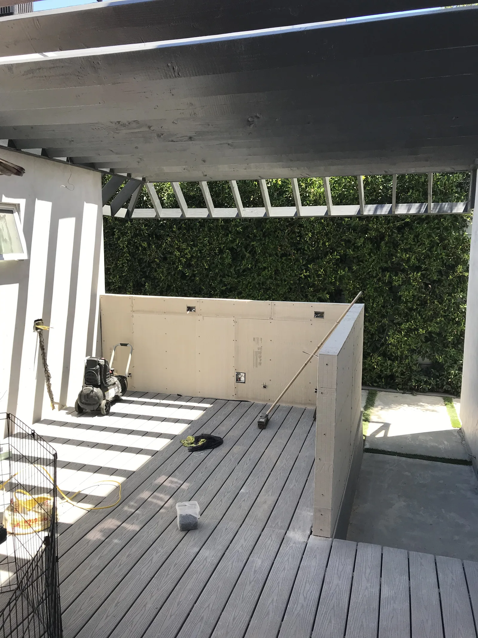A cement board wall for a kitchen structure, with an extended pergola overhead