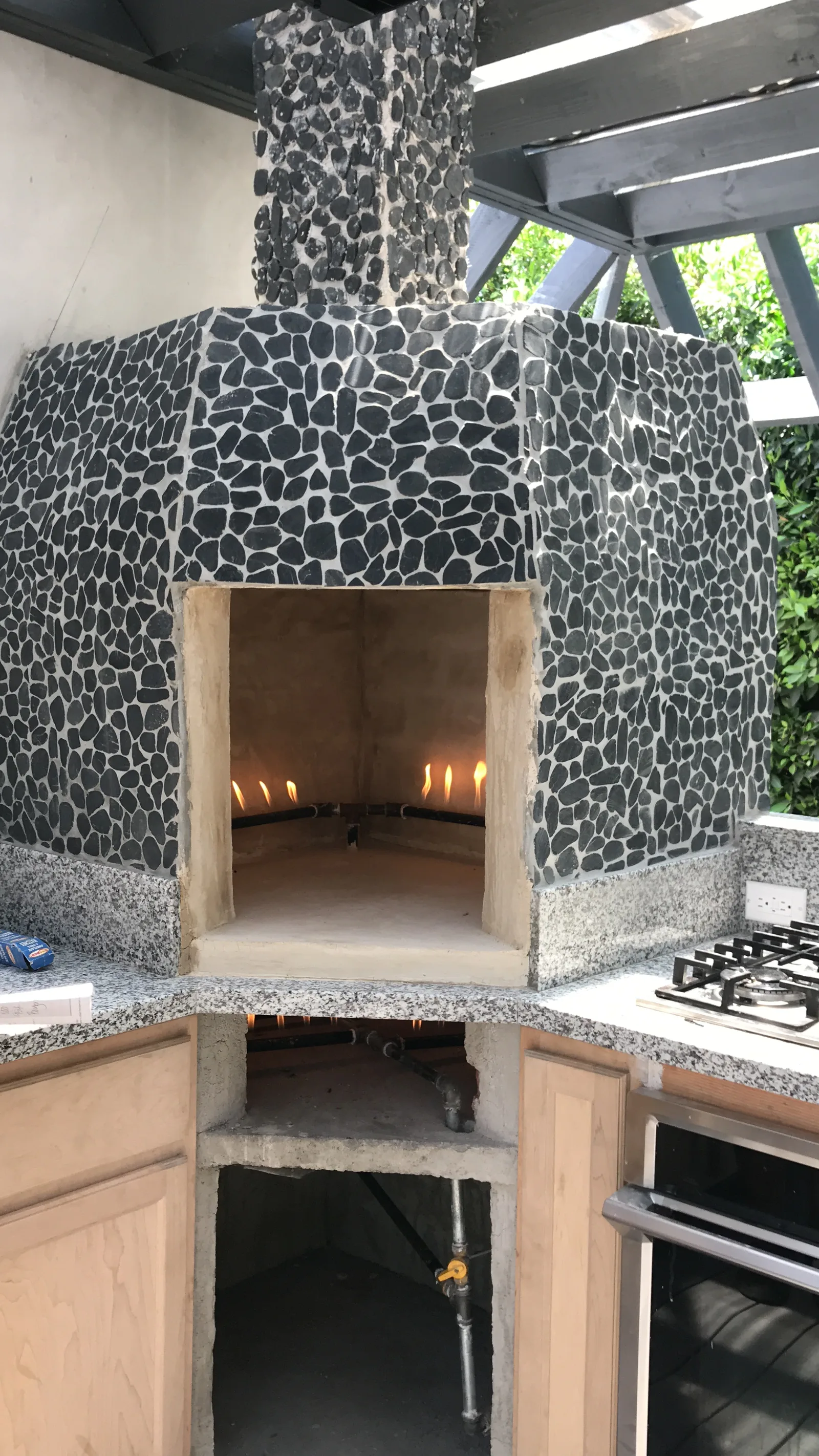 A finished oven structure, lit, with a gas cooktop alongside it