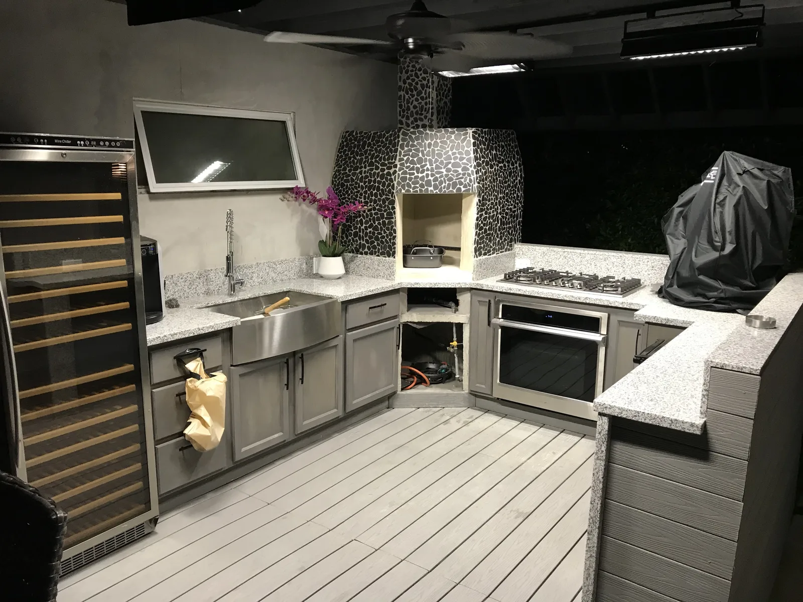 The finished outdoor kitchen with stained cabinets, a wine fridge, and the oven complete