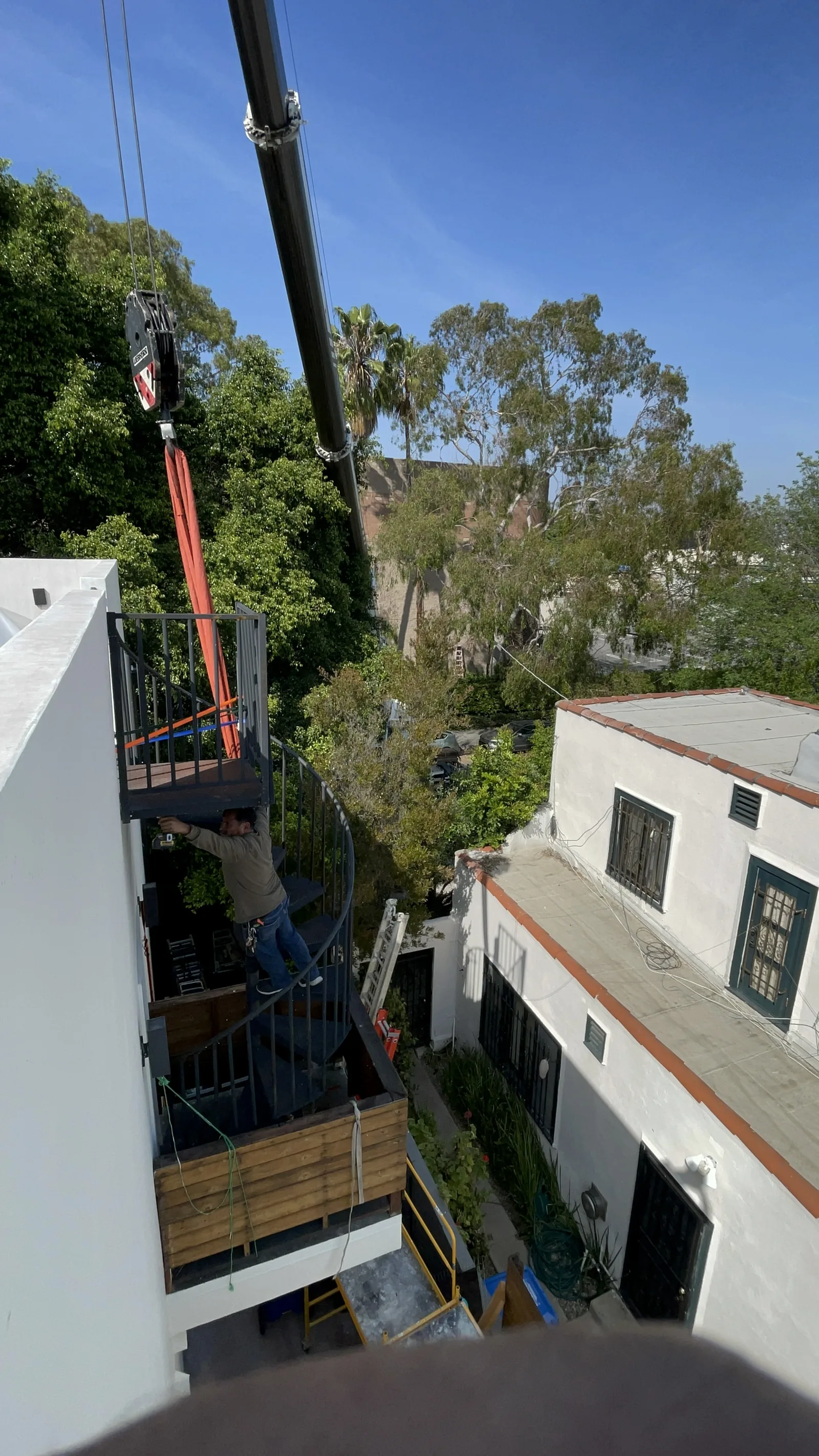 A worker riding a crane-suspended platform beside the balcony structure, with the wood-clad deck visible below