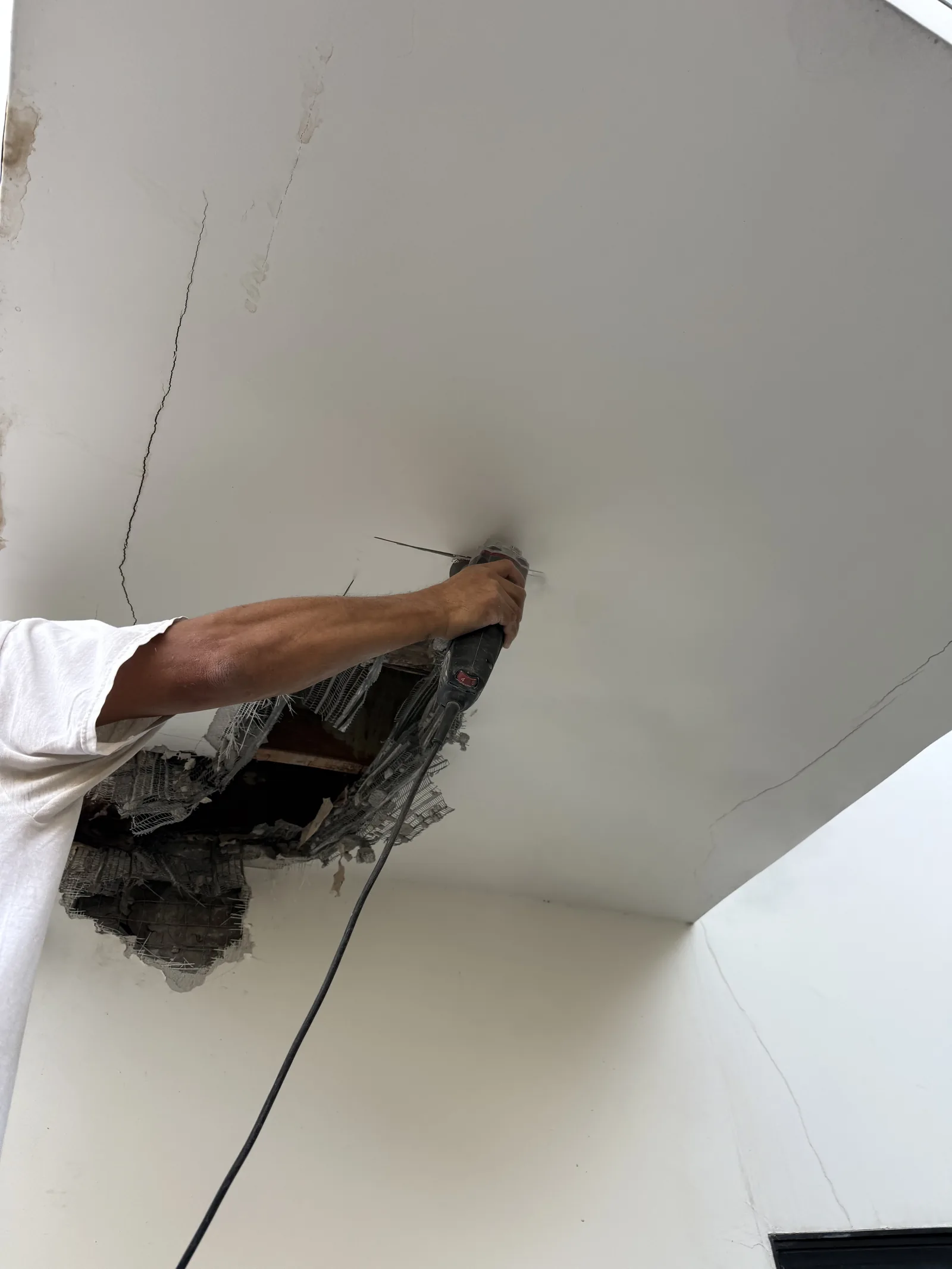 A worker cutting into a cracked ceiling to access water damage above