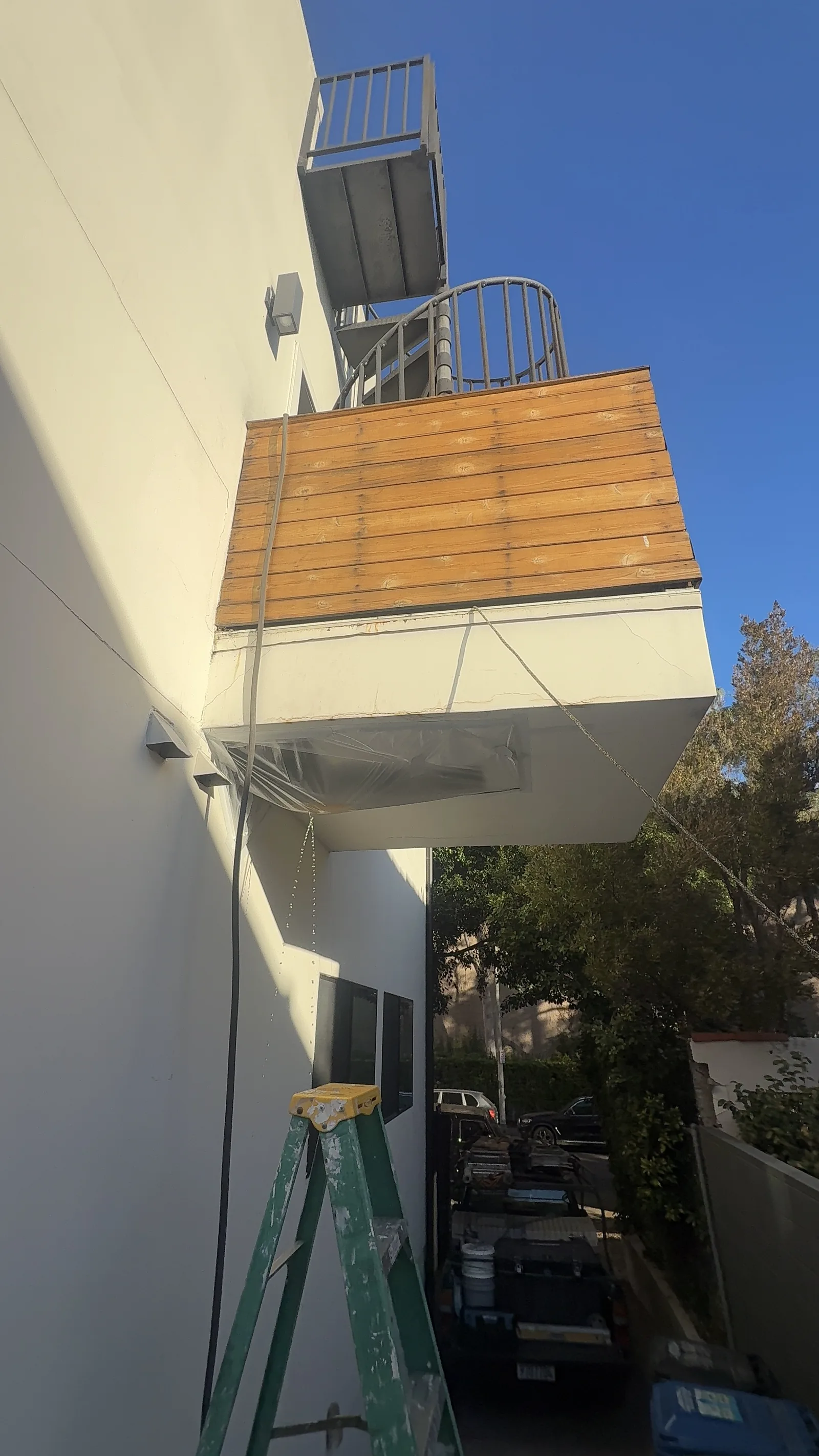 The underside of the balcony with new wood cladding installed, viewed from below with a ladder in place