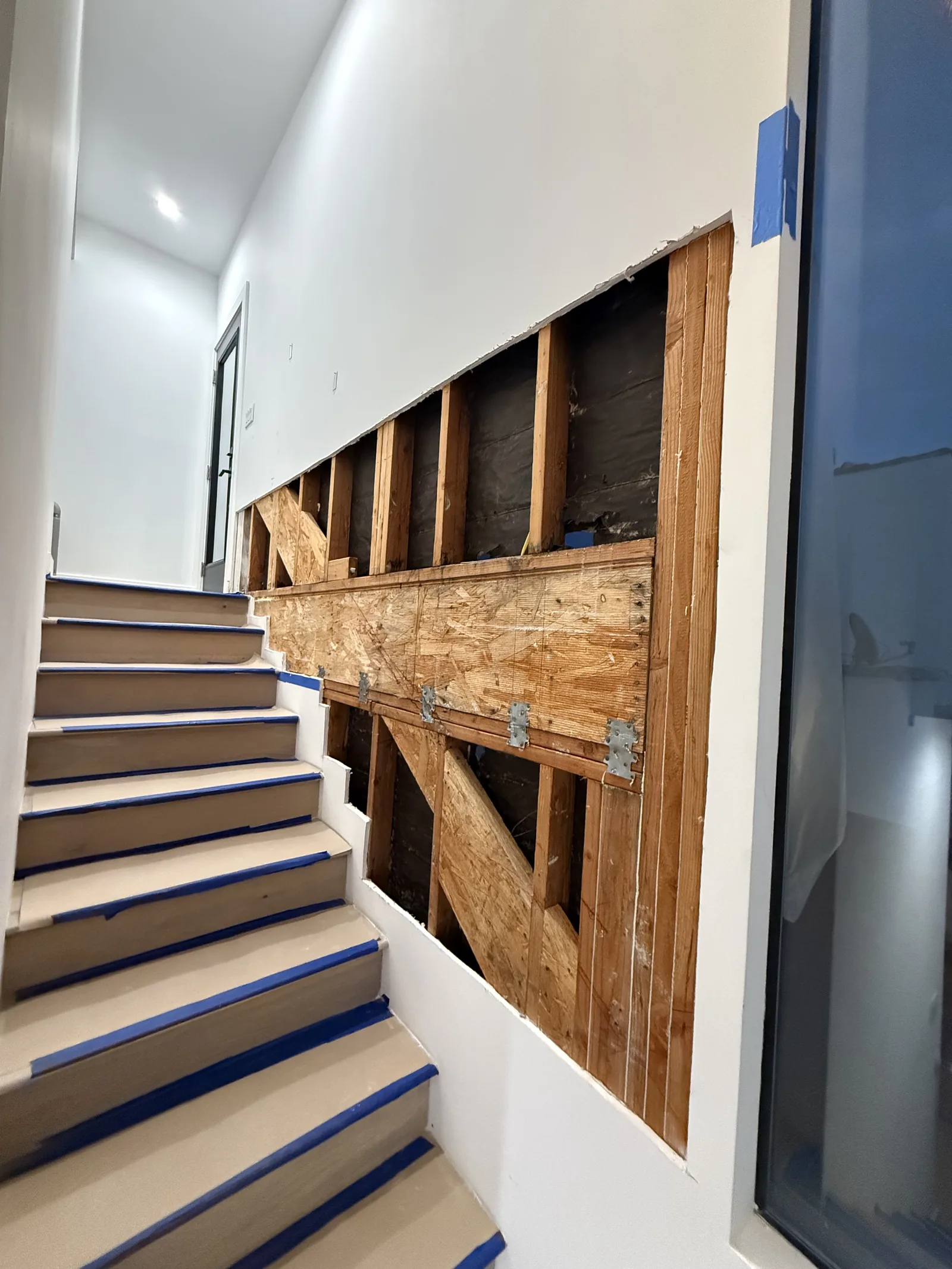 An interior stairwell wall opened to the studs beside a protected staircase