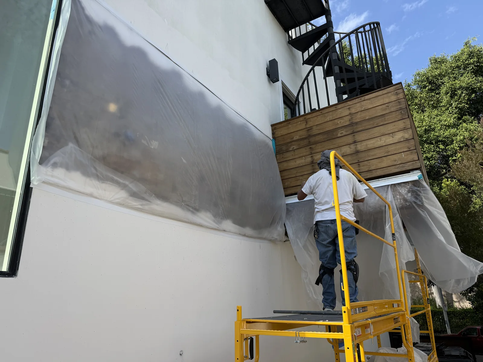 A worker on a scaffold applying a coating to an exterior wall