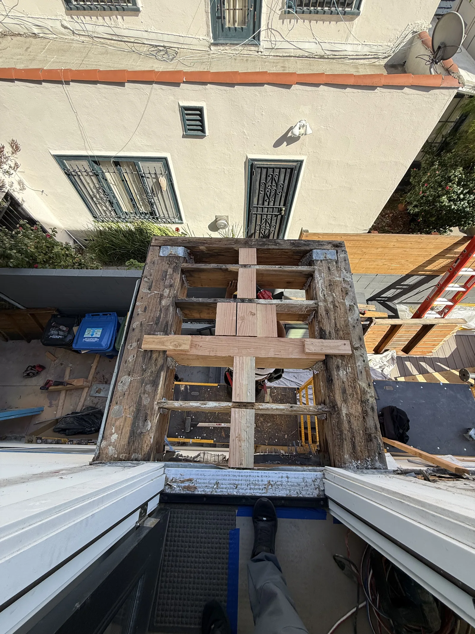 A wider view of the balcony framing skeleton with tools and a ladder visible on the roof below