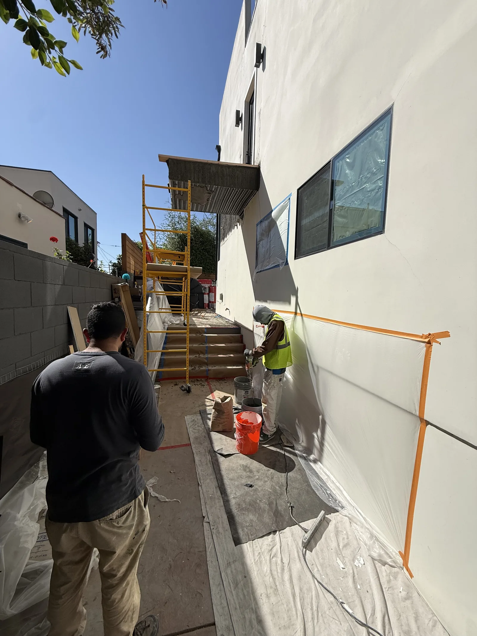 A worker applying a waterproof membrane to the exterior wall beneath the balcony