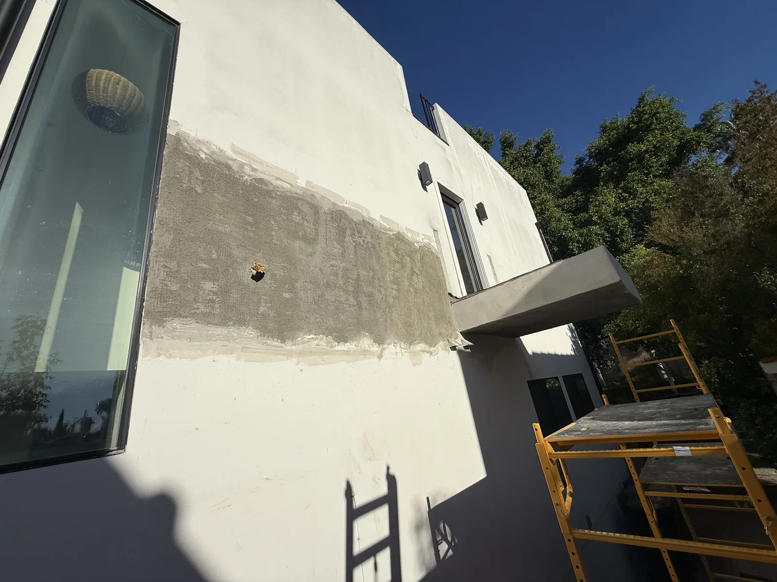 The stucco crack repair mid-progress on the exterior wall, with a ladder and scaffold in place