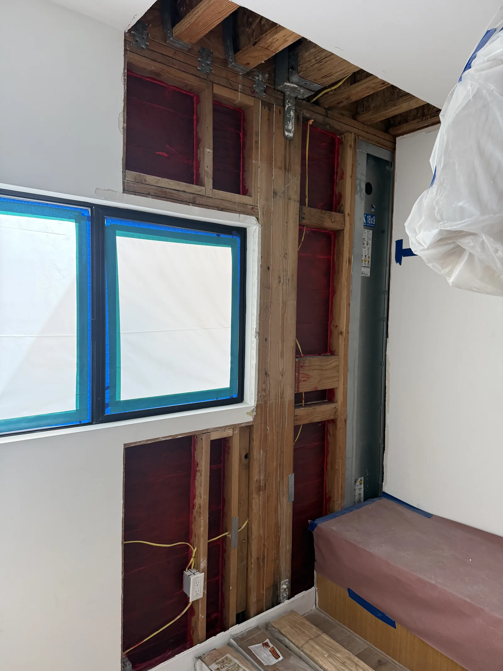 An interior wall opened near a window down to the studs, with a built-in bench protected below