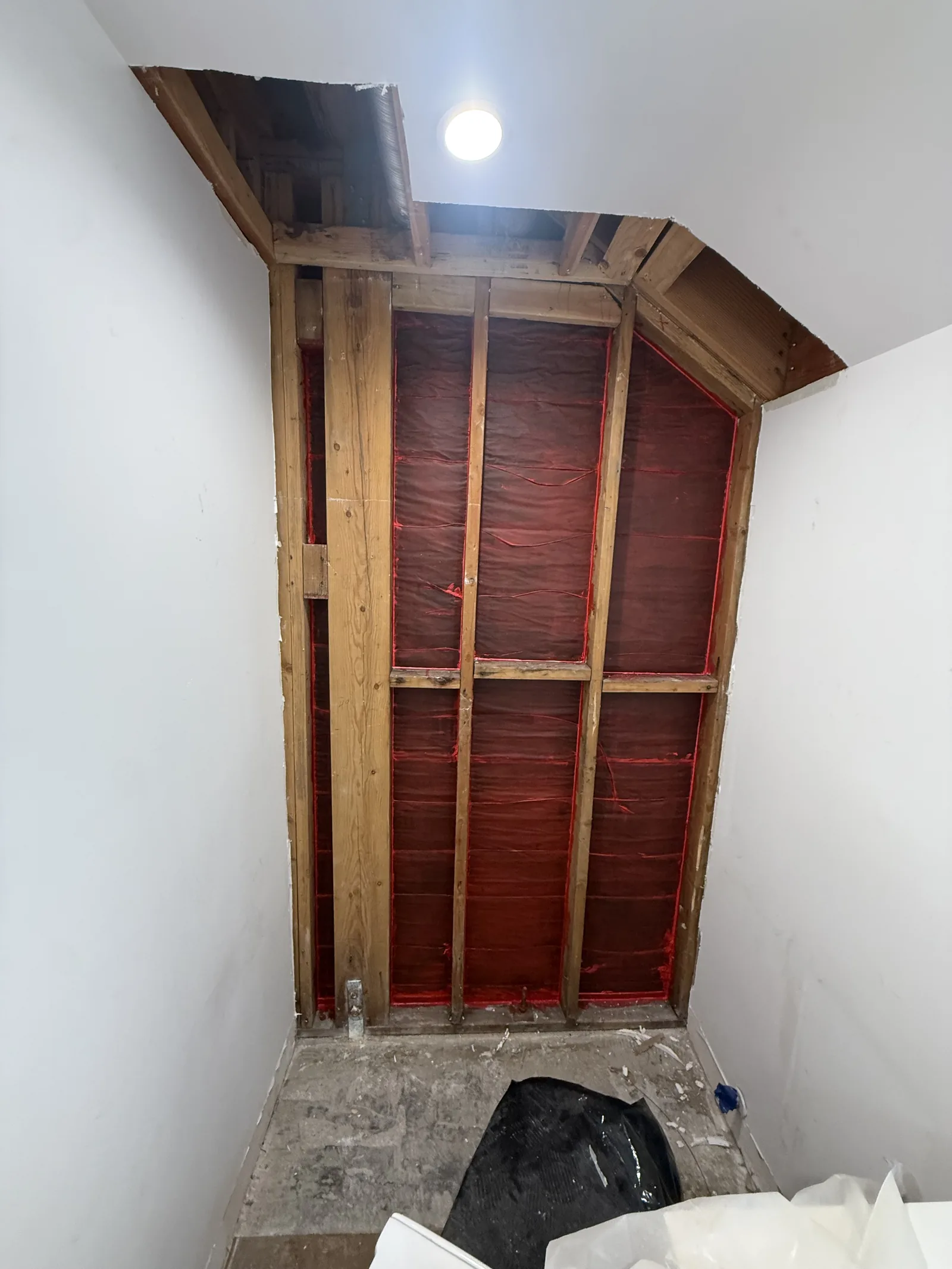 A closet or stairwell wall opened down to the studs, with a plumbing stub visible at the floor